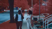 Two people walking down a sidewalk with red leaves on the trees